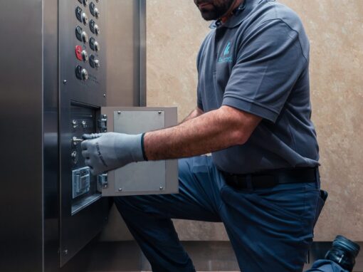 A maintenance worker kneeling and adjusting the elevator control switches in a stainless steel panel.
