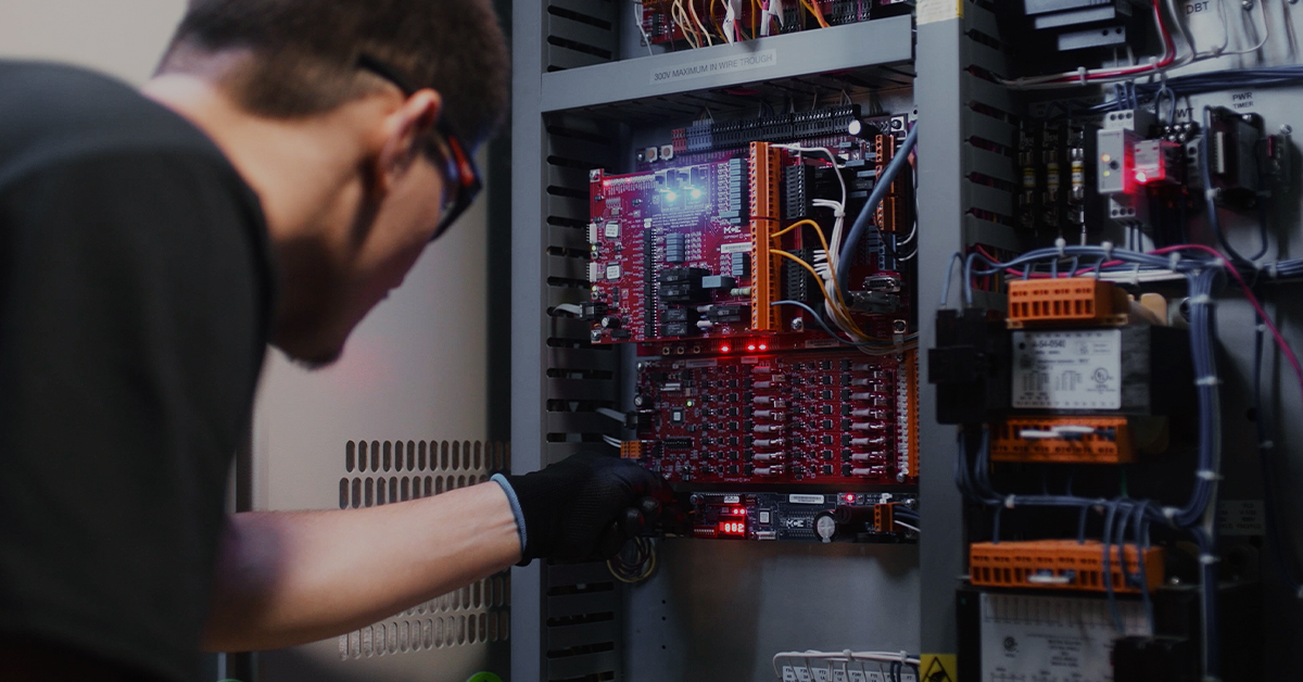 A focused technician troubleshooting an elevator's red control board with LED indicators.