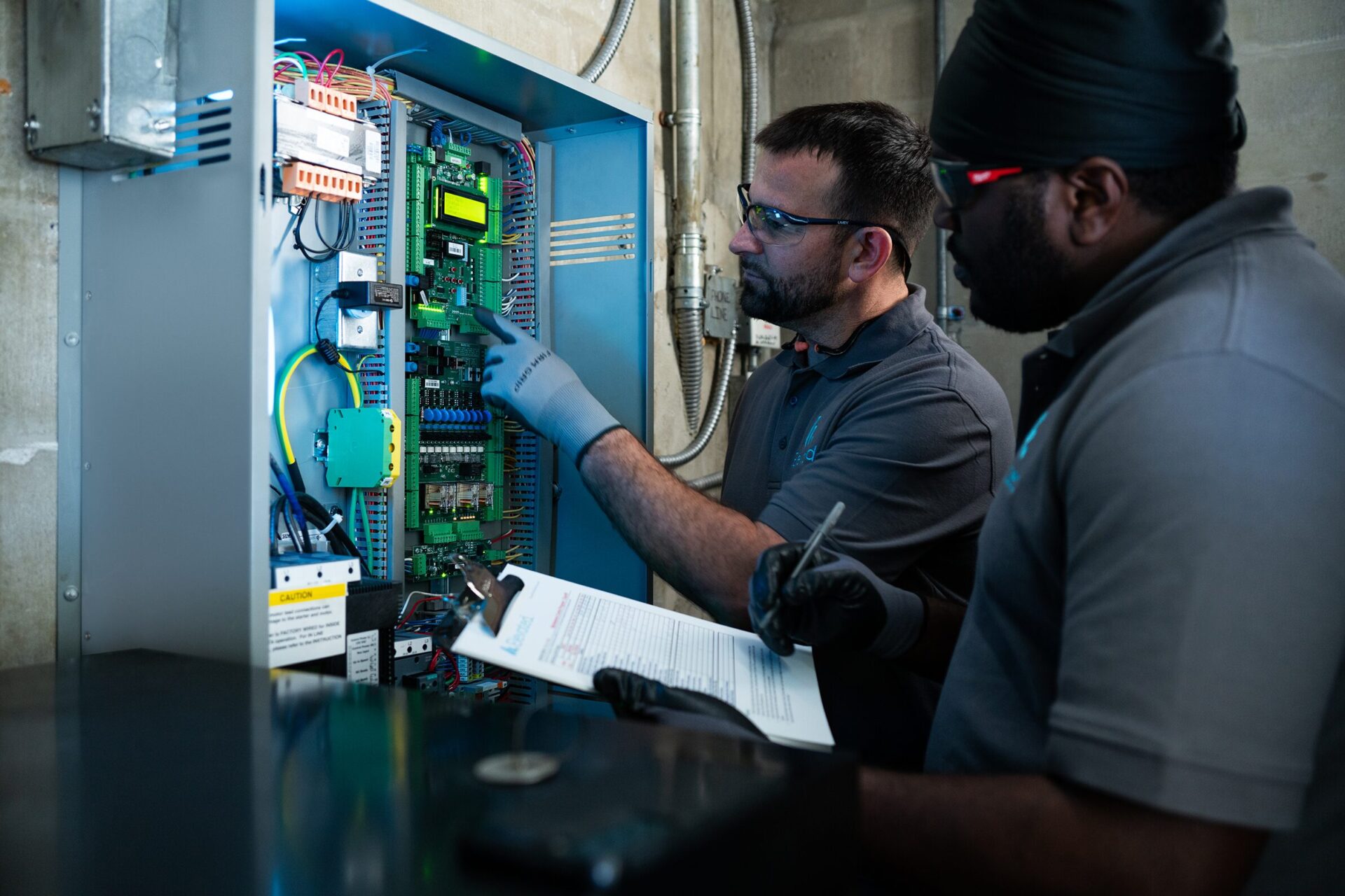A maintenance worker kneeling and adjusting the elevator control switches in a stainless steel panel.