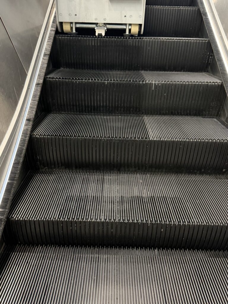Close-up of black escalator steps and grooves, showing the tread surface and risers in detail.